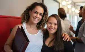 Woman with down syndrome standing with Hispanic woman in white top smiling