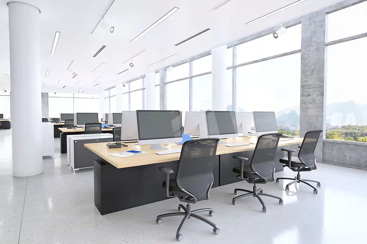 Rows of workstations in a large office space, near tall windows with a landscape view.