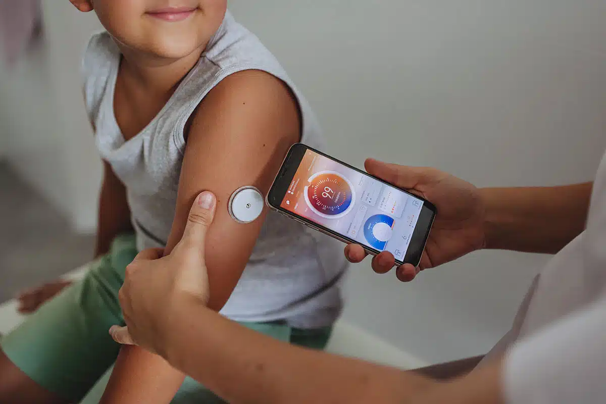 A young boy in a doctor’s office has the data from his continuous glucose monitor, displayed on an iPhone, read by a medical professional.