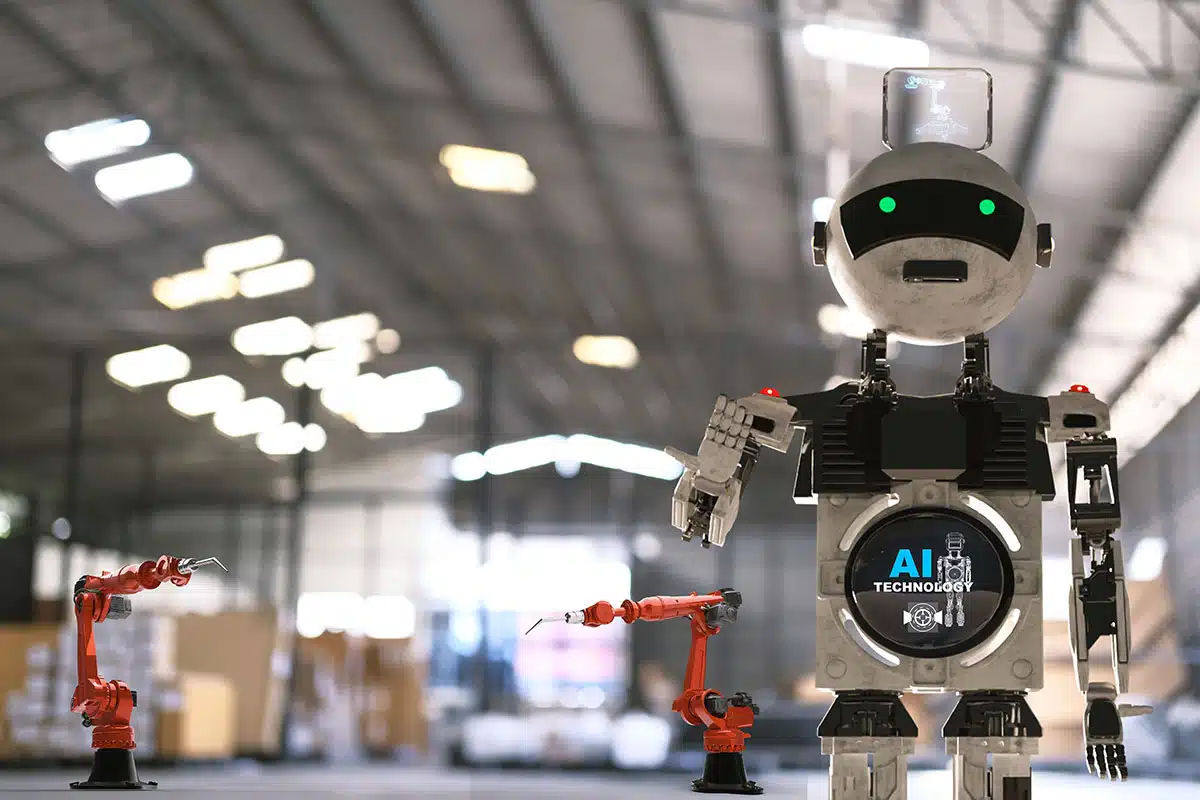 A robot stands next to a couple of pieces of equipment in a large warehouse.