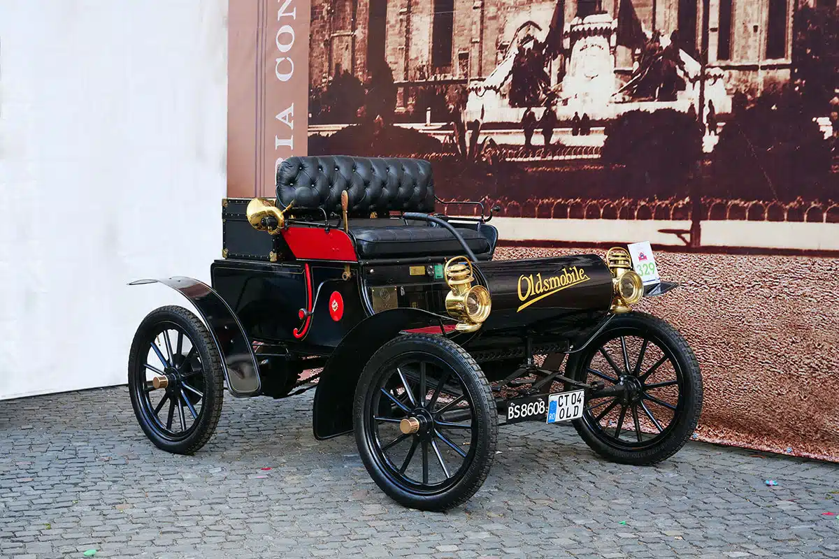 An early 1900s model of the Oldsmobile Curved Dash, parked outside.