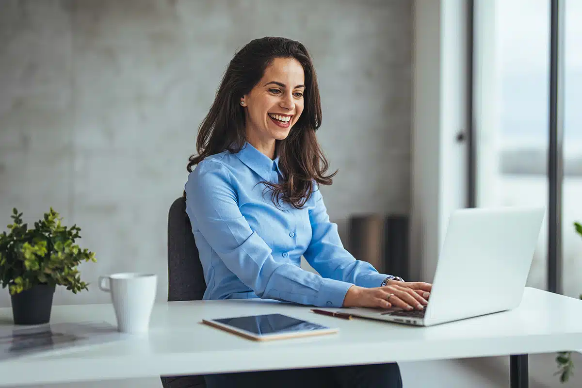 A woman in a blue, button-down shirt, seated at a desk in a pristine office environment