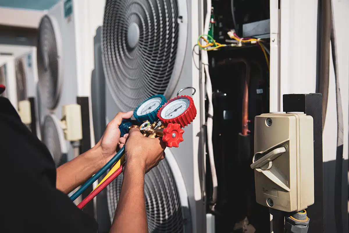 A close-up view of someone outdoors, holding a meter next to an HVAC system